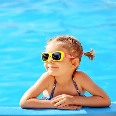 Малко дете се усмихва в края на басейн. Твърдостта на водата в басейни може да повреди повърхностите на басейна и да предизвика корозия на тръбите.